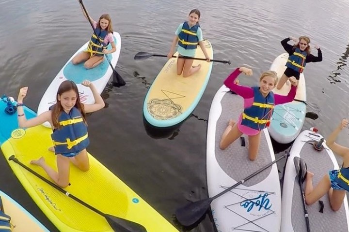 Young girls in life vests flexing their arms on paddle boards