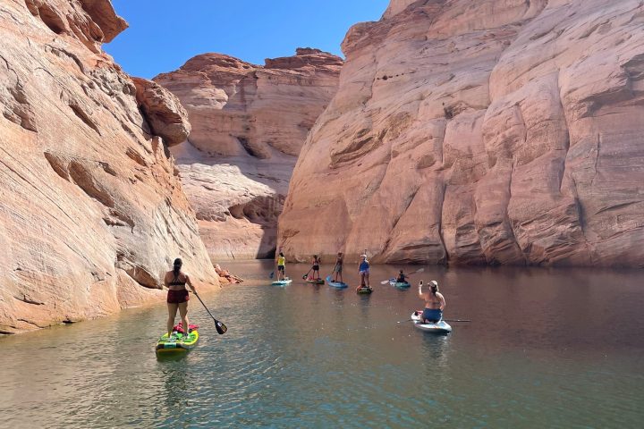 a group of people on a rock next to a body of water with Lake Powell in the background