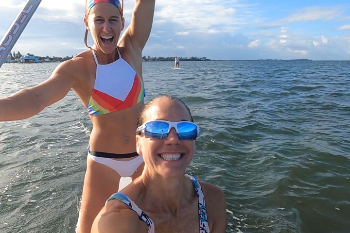 a person wearing a hat and sunglasses posing near a body of water