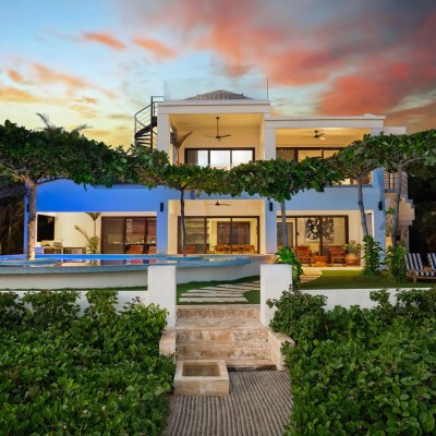 Modern villa with pool at sunset, surrounded by greenery and vibrant skies.