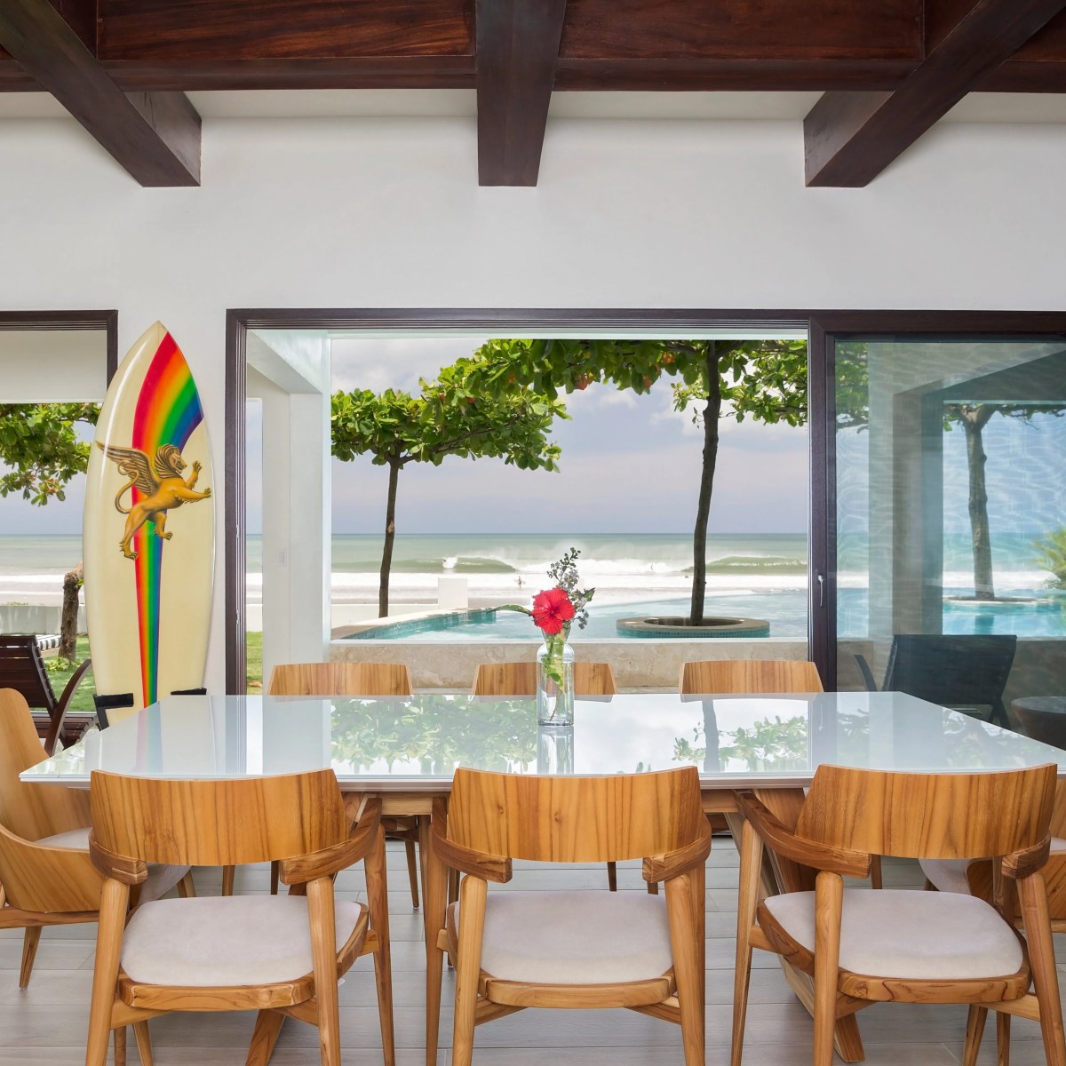 Dining room with wooden chairs, surfboard, ocean view, and sliding glass doors.