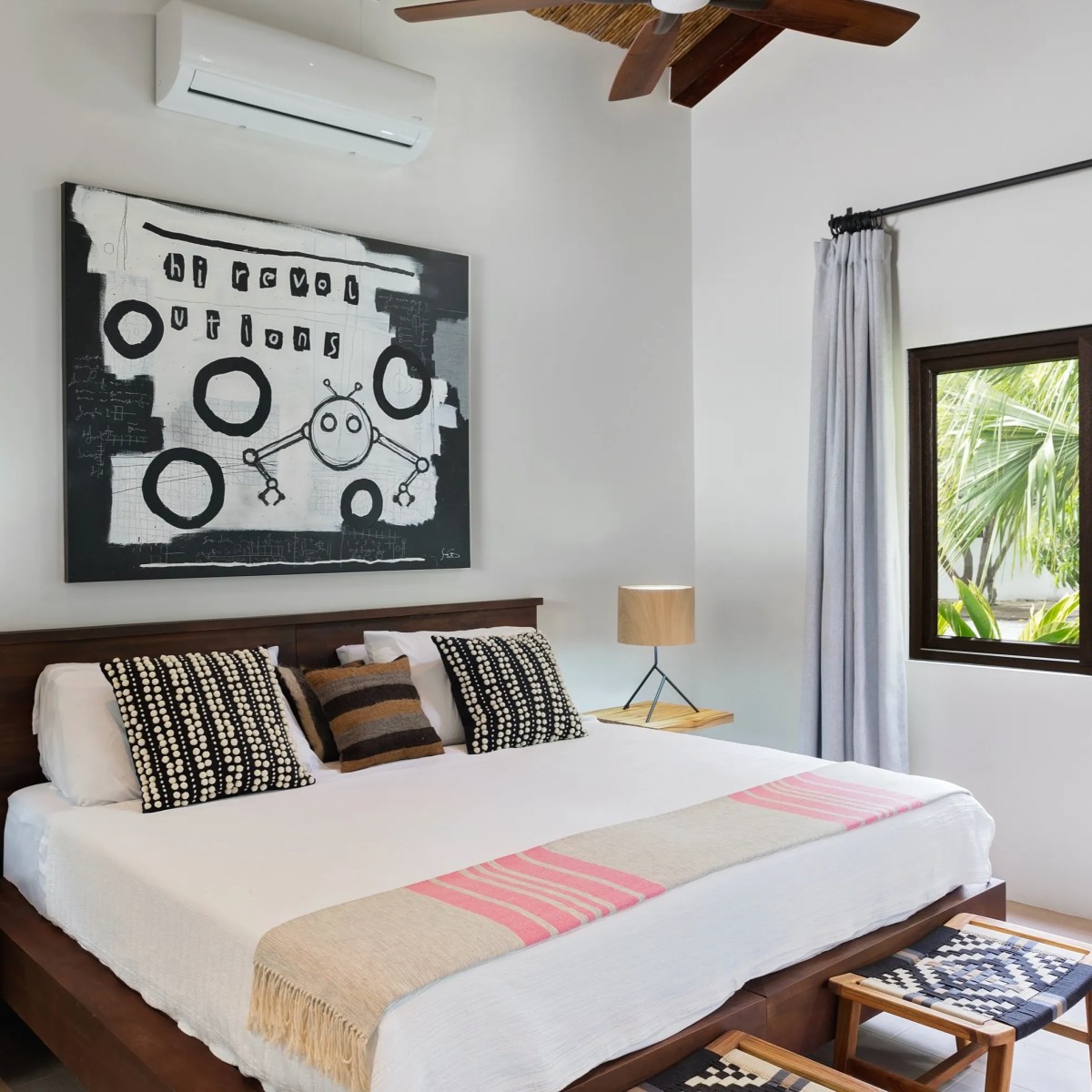 Modern bedroom with abstract art, wooden bed, matching side tables, and a window with tropical view.