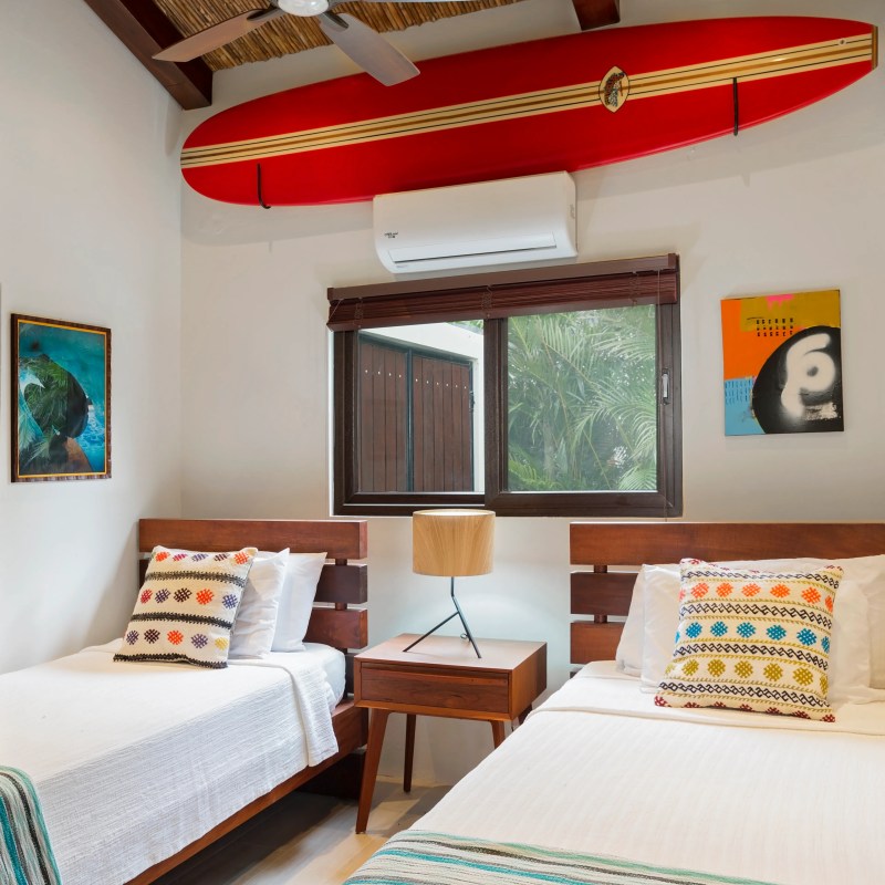 Bedroom with twin beds, red surfboard on ceiling, and colorful decor.