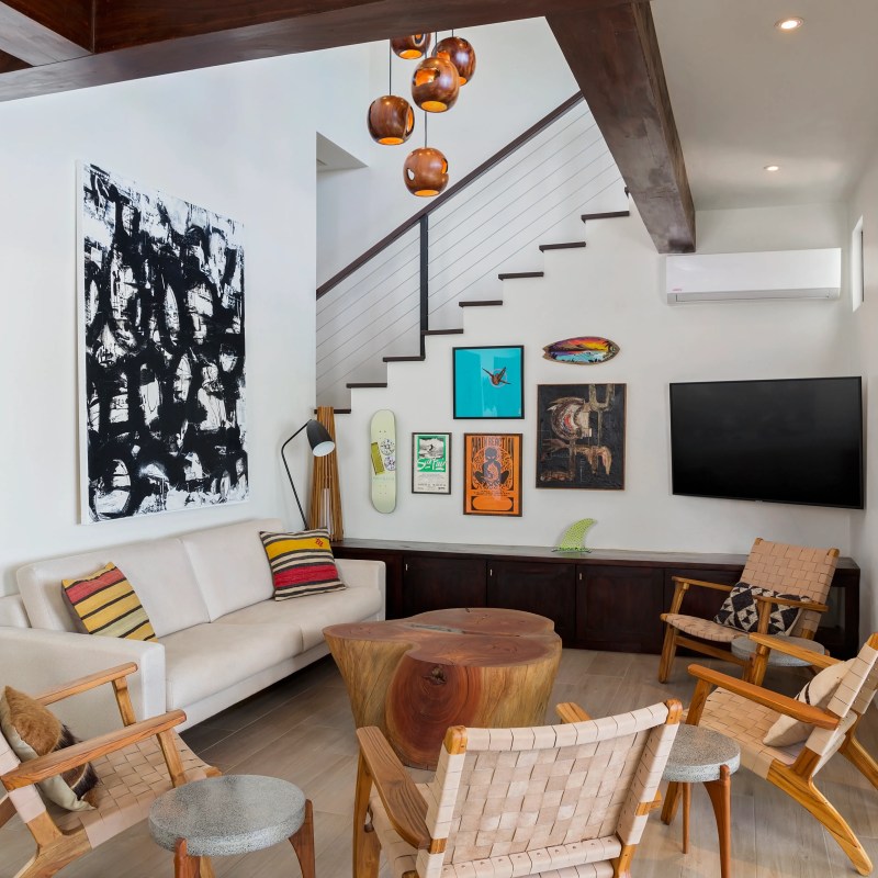 Modern living room with art, wooden furniture, TV, and staircase.