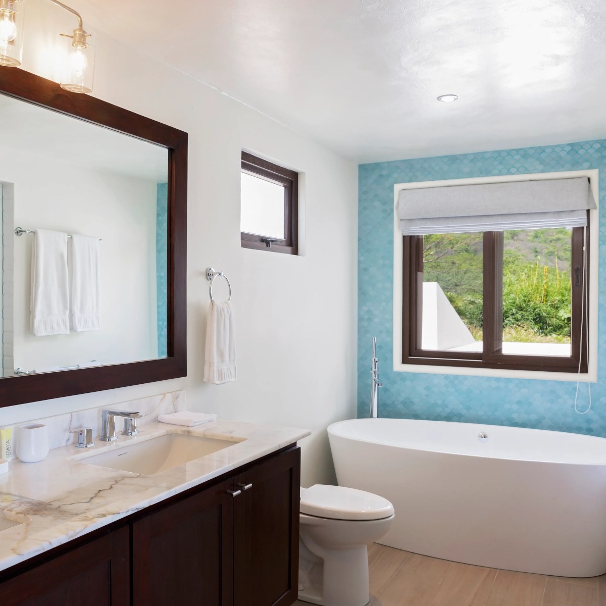 Modern bathroom with double sink, large mirror, freestanding tub, and turquoise-tiled walls.