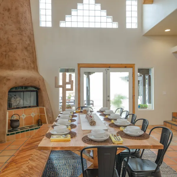 Dining room with a long wooden table, chairs, and a large clay fireplace.