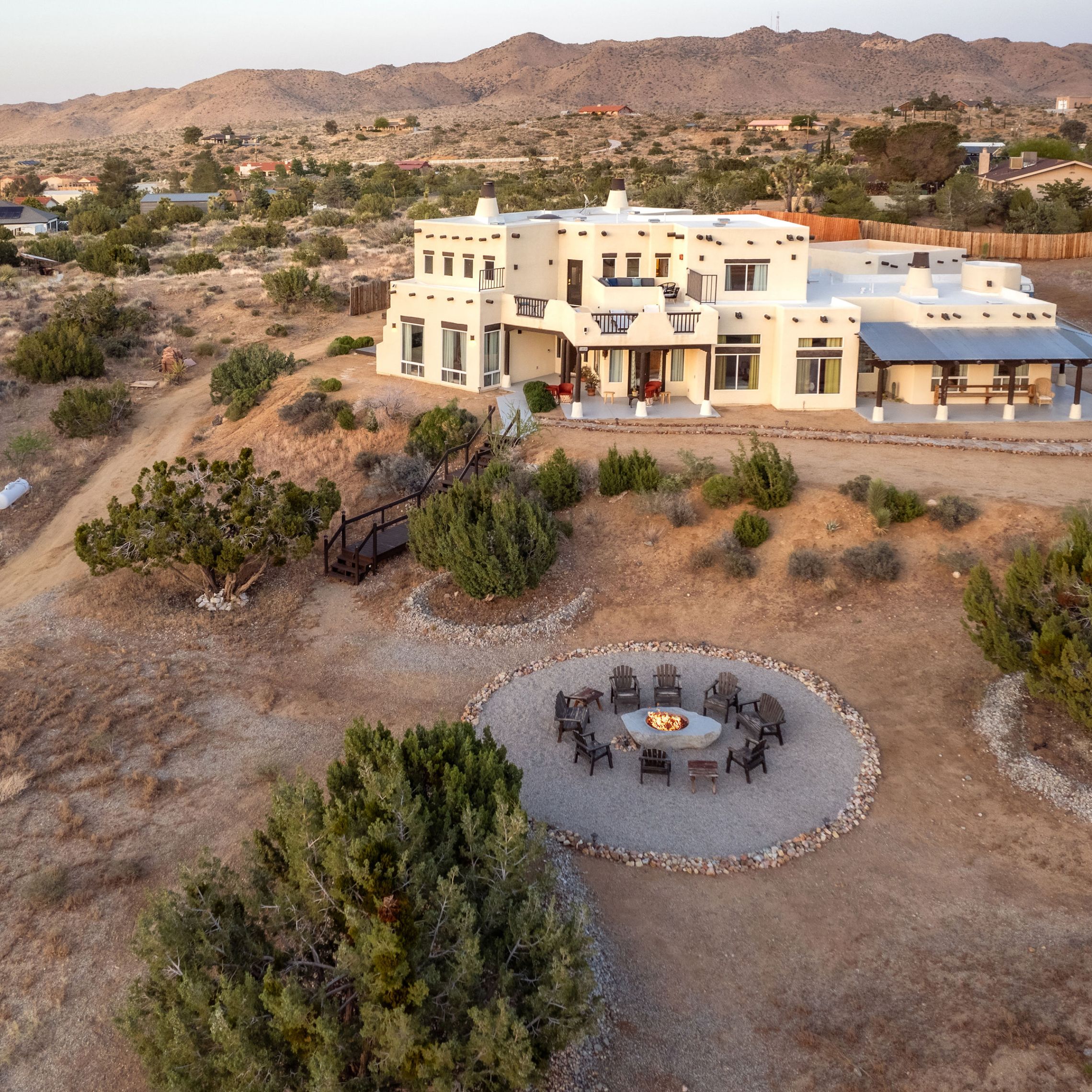Desert landscape with a white house and circular fire pit area surrounded by chairs.
