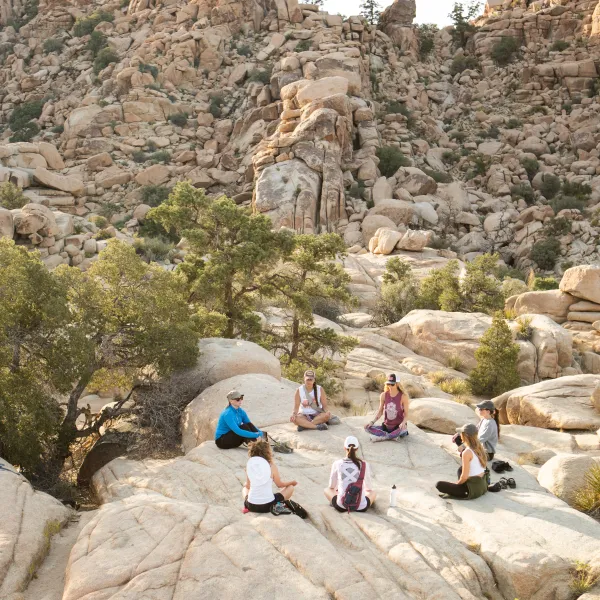 Group of people meditating on rocky terrain in a desert landscape.