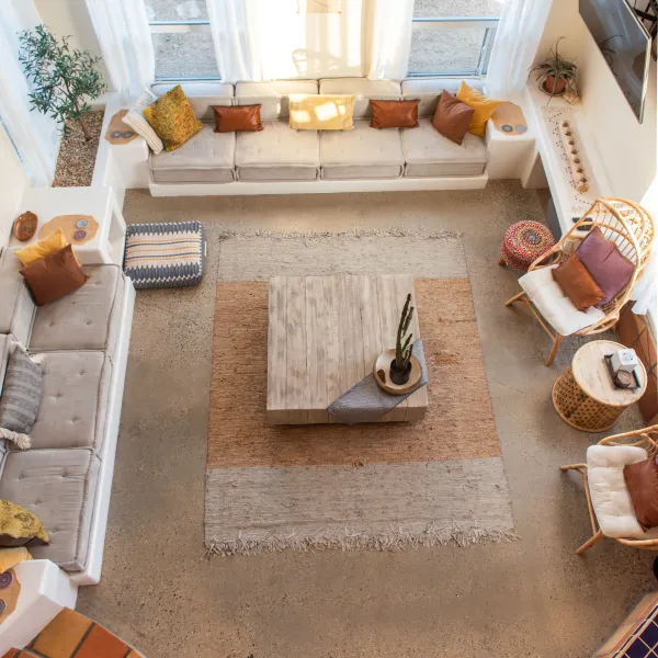 Aerial view of a cozy living room with a large window, cushioned seating, wooden table, and decorative cushions.