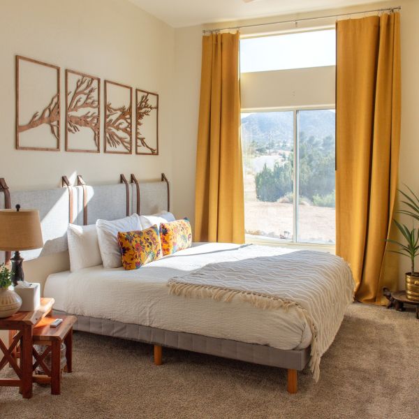 Cozy bedroom with a large window, yellow curtains, and a neatly made bed.