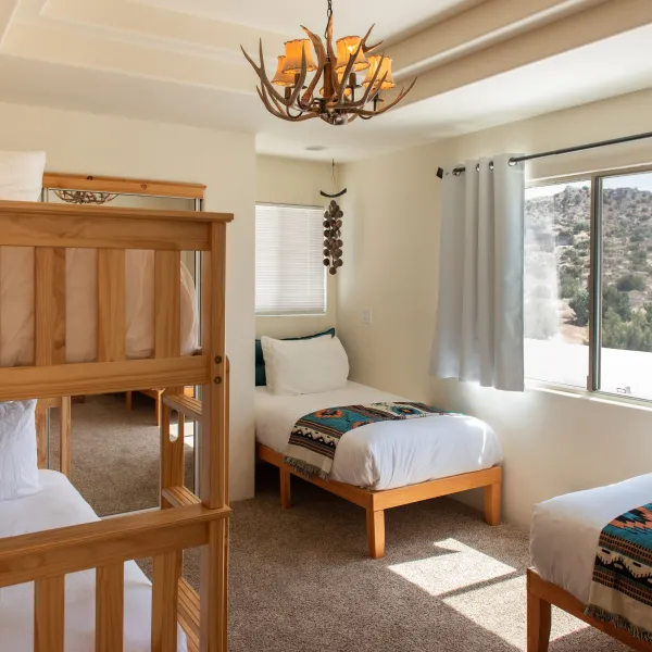 Bedroom with bunk beds, two single beds, antler chandelier, and mountain view from the window.