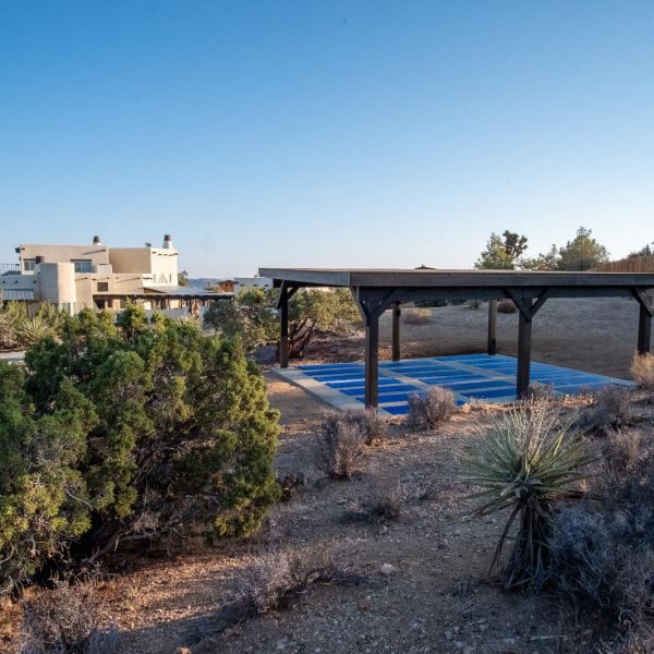 House and shaded area in desert landscape with clear sky background.