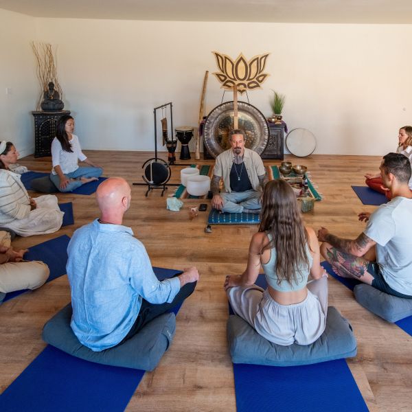 Group meditation session with leader in room with musical instruments and a large gong.