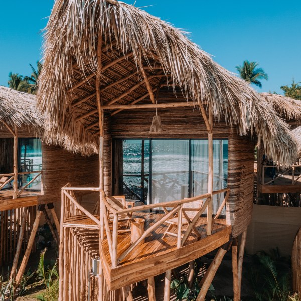 Tropical huts with thatched roofs and wooden balconies under a clear blue sky.