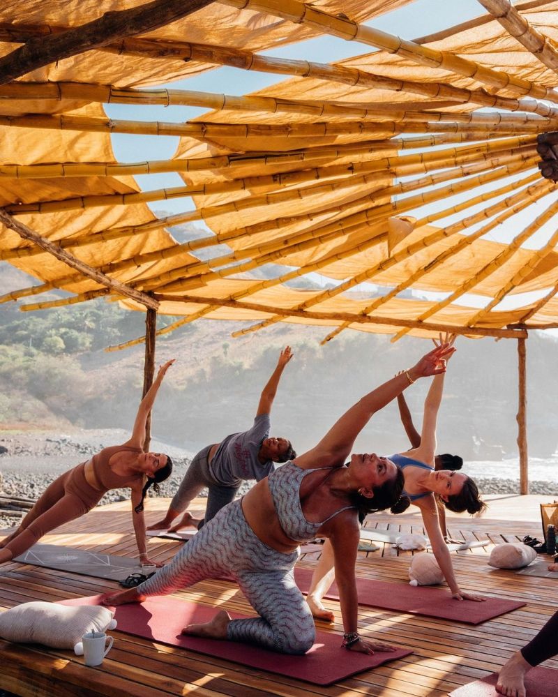 PlacesOfHealing_Mizata09 People practicing yoga outdoors on mats under a bamboo canopy.