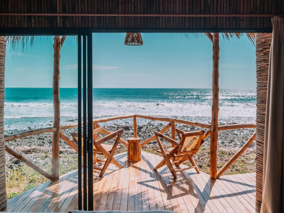 View of ocean from a wooden deck with two chairs through an open sliding door.