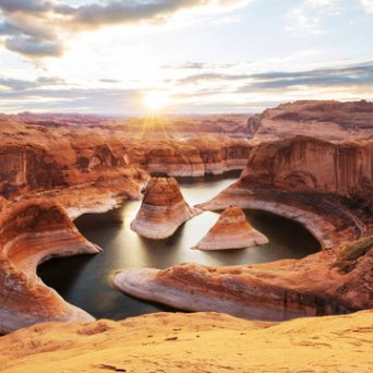 Sunset over Horseshoe Bend, with a river winding through red rock canyons under a cloudy sky.