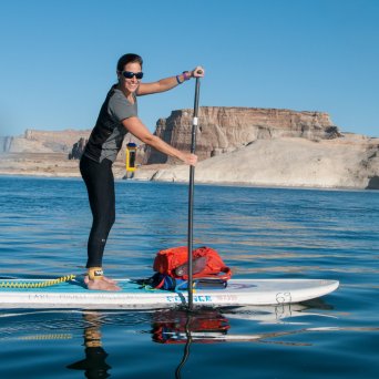 Person paddleboarding on a lake with rocky cliffs in the background, under a clear blue sky.