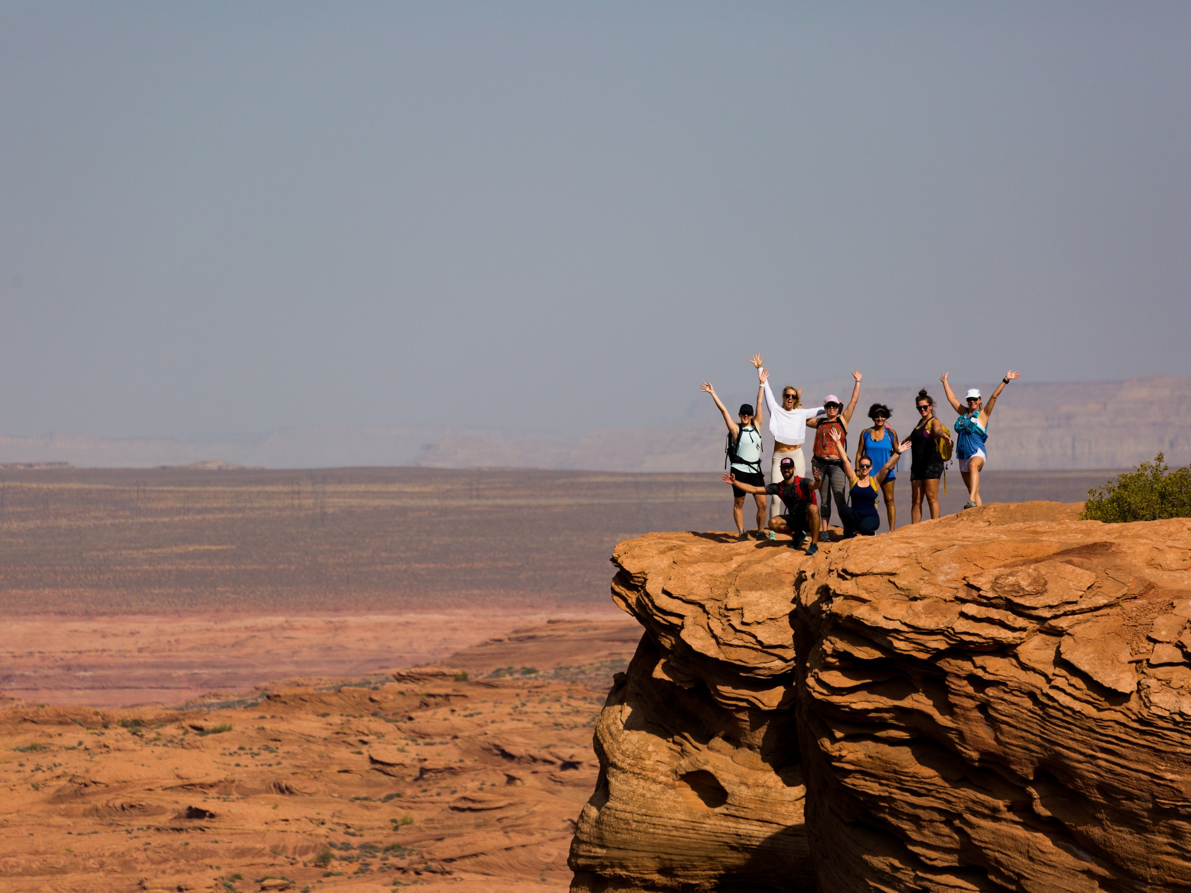 Group of people raising arms on a rocky cliff in a desert landscape.