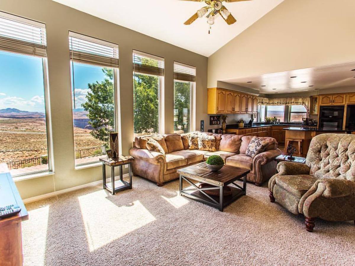Spacious living room with large windows, brown couches, and an open kitchen view.