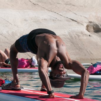 Person doing a yoga backbend on a paddleboard in a rocky water setting.