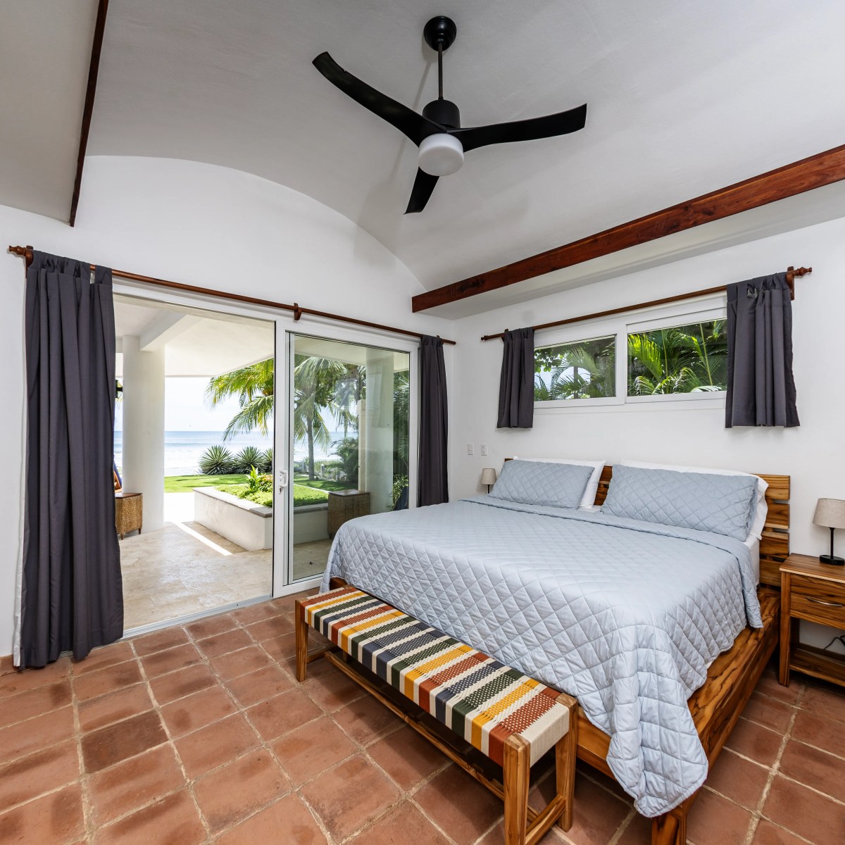 Bedroom with blue bedding, ceiling fan, and open sliding glass doors to ocean view.