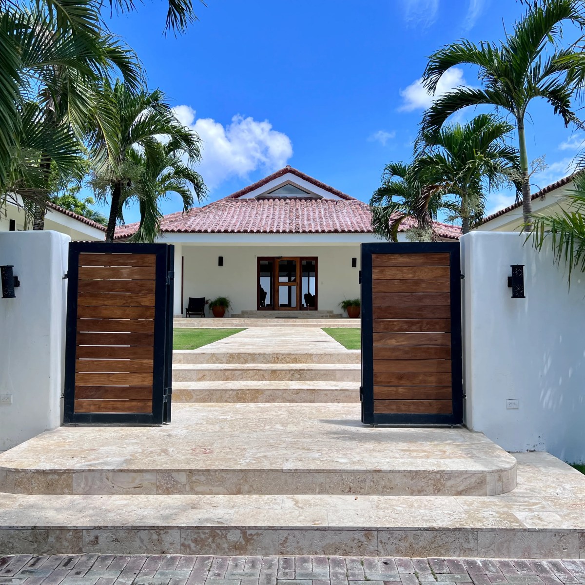 Entrance to a modern house with red-tiled roof, flanked by palm trees.