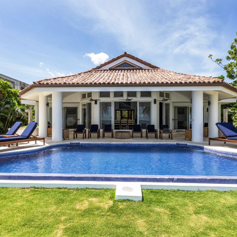 Luxury house with tiled roof and pool, surrounded by greenery and blue sky.