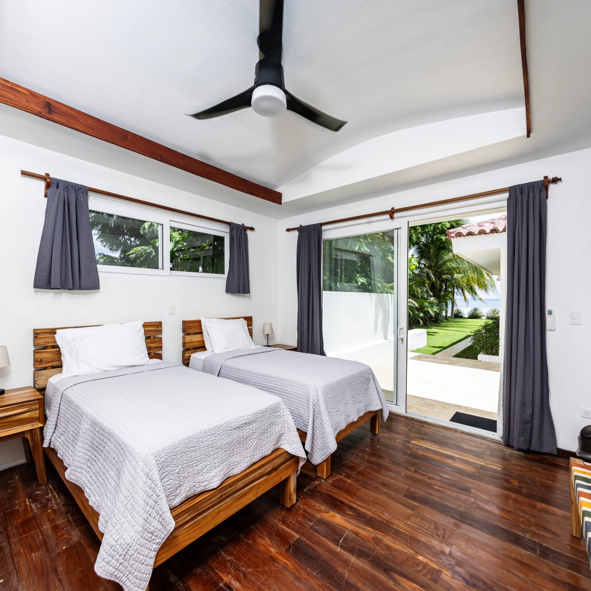 Two beds in a bright room with wood flooring, open sliding door, and garden view.