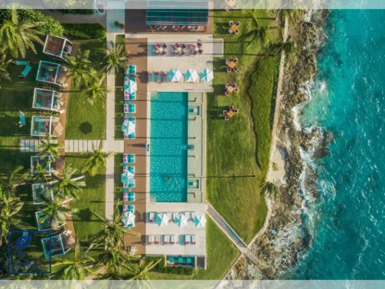 Aerial view of a beachfront pool area, with loungers and umbrellas, next to the ocean.