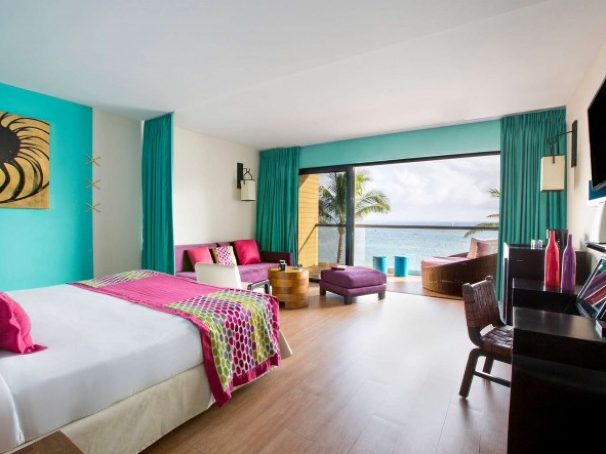 Bright hotel room with ocean view, colorful decor, balcony, and seating area.