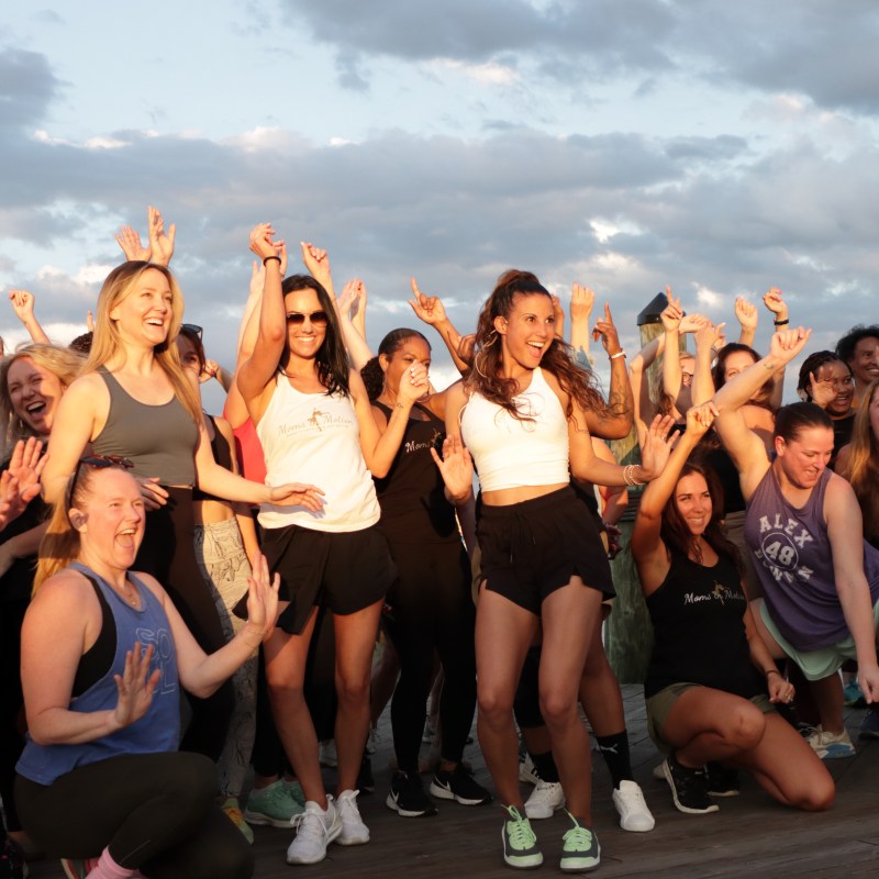 Group of smiling people posing energetically outdoors under a cloudy sky during sunset.