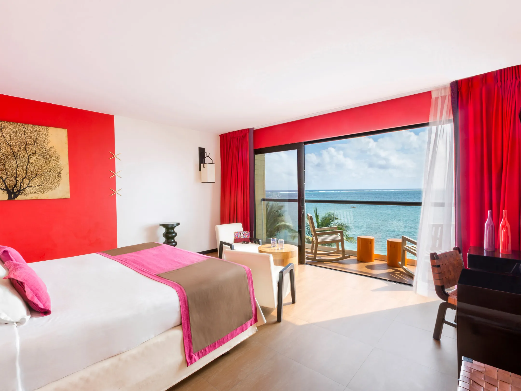 Bright hotel room with ocean view, red accents, and modern decor.
