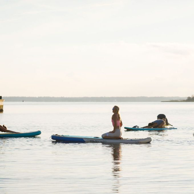 People practicing yoga on paddleboards in calm water near a pier.
