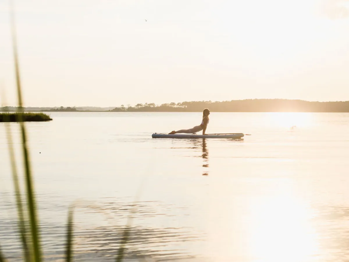 Person doing yoga on a paddleboard in a calm lake at sunset.