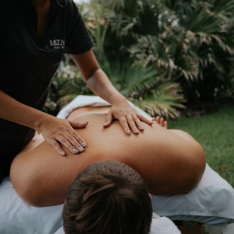Person receiving a back massage outdoors on a massage table near greenery.