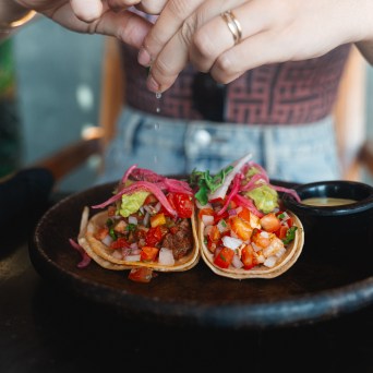 Person squeezing lime over two tacos on a black plate.