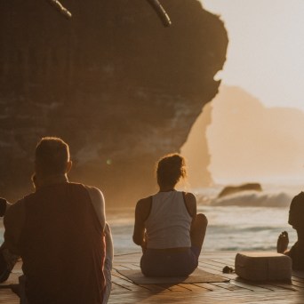 People sitting on a deck by the sea at sunset, with cliffs in the background.