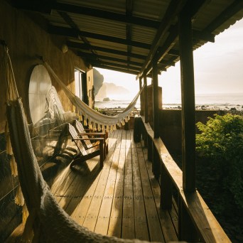 Wooden porch with hammocks overlooking a misty coastline at sunrise.