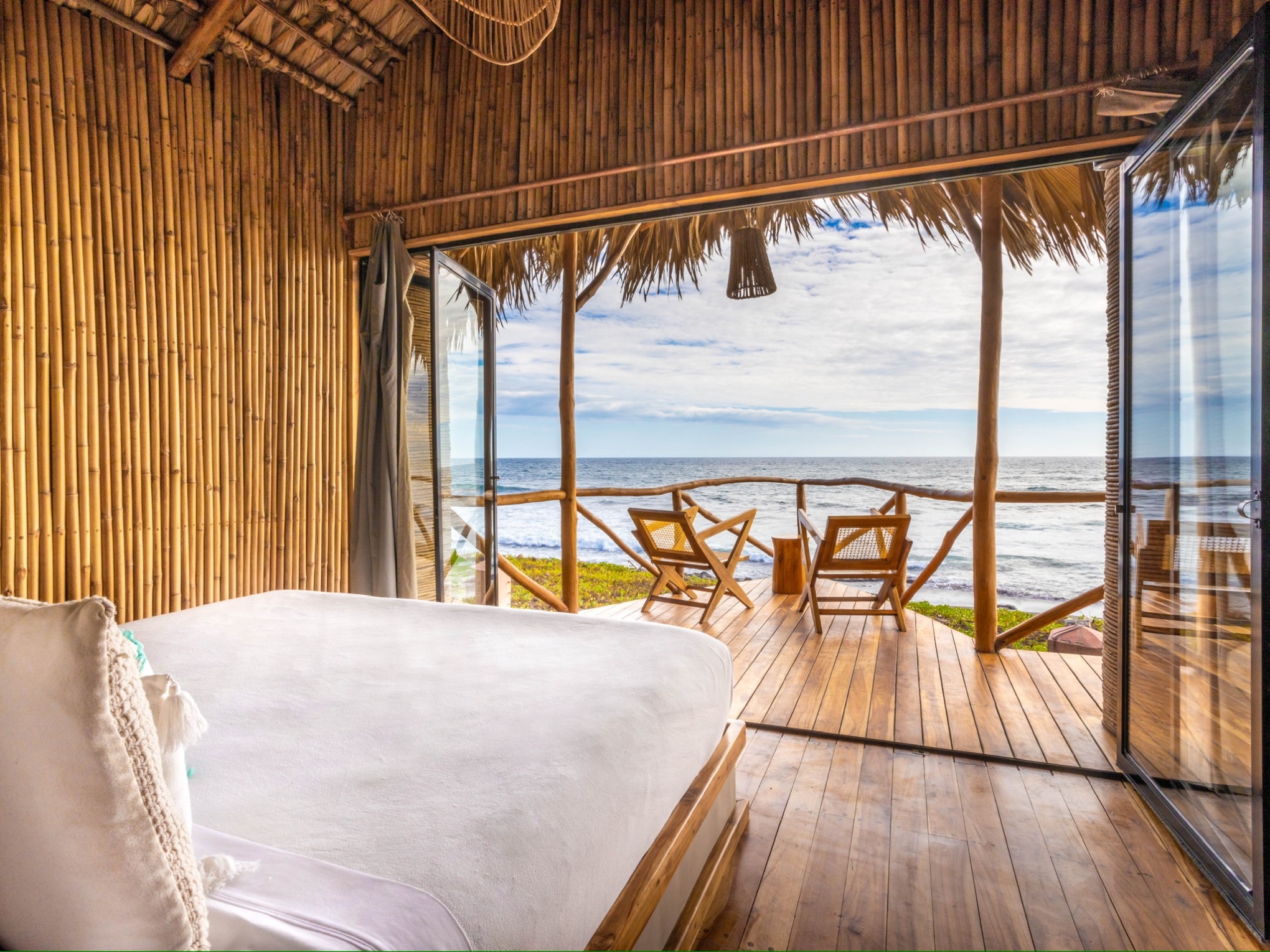 Beachside bamboo room with open doors to ocean view and two chairs on deck.