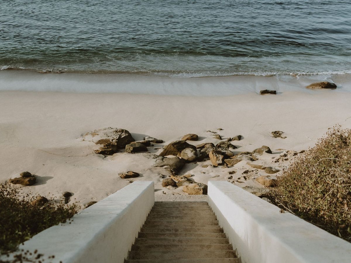 Stone steps leading down to a sandy beach with ocean view.