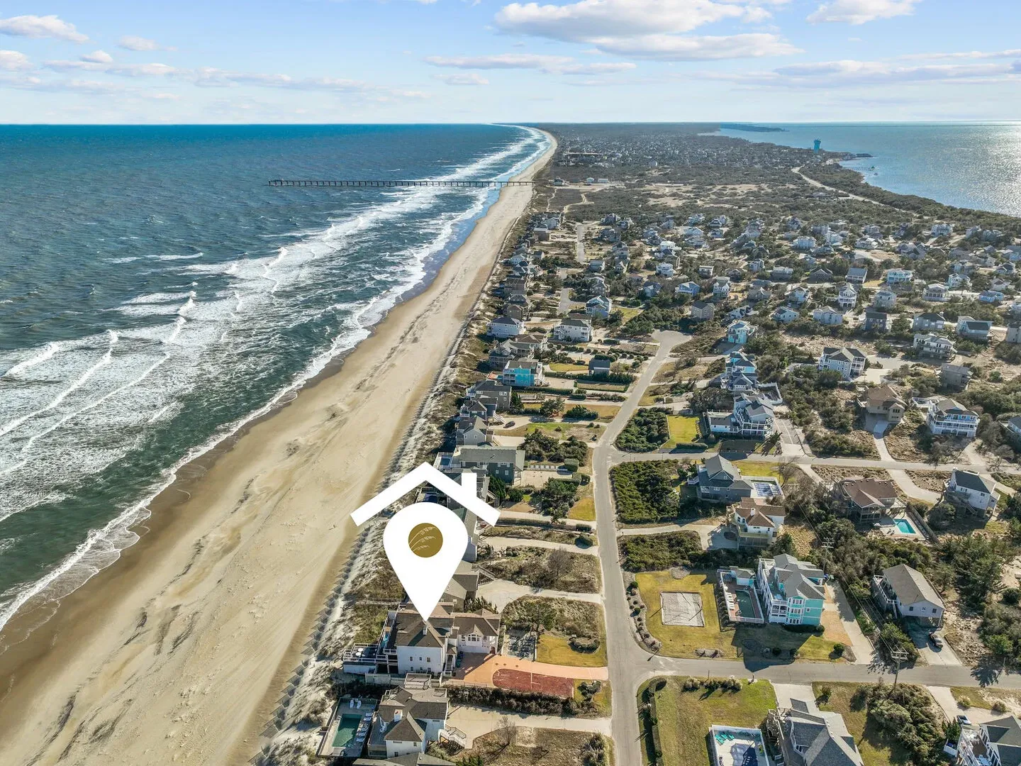 Aerial view of a coastal town with a beach, ocean, houses, and a digital map marker icon.