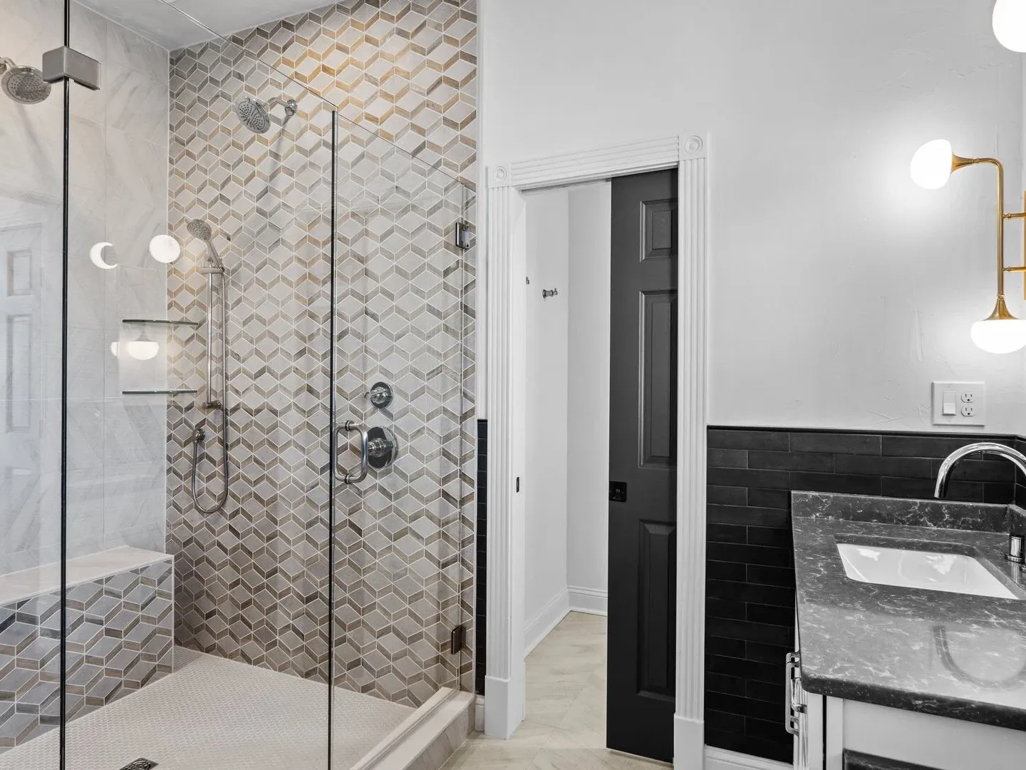 Modern bathroom with glass shower, geometric tiles, black vanity, and globe wall lights.