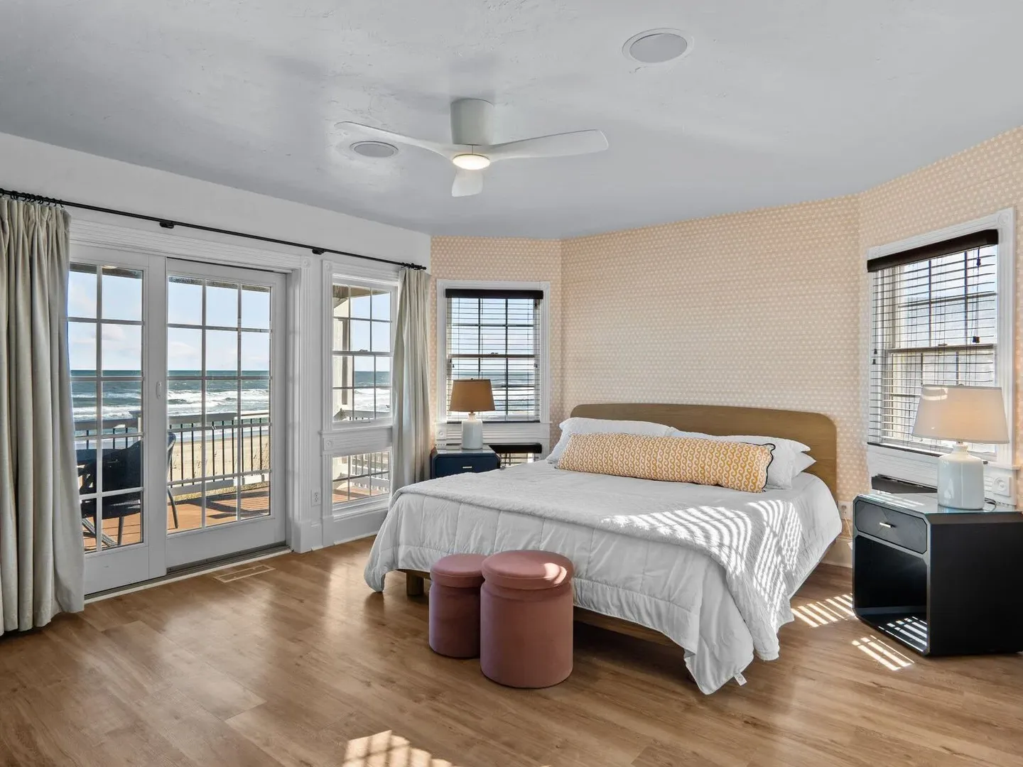 Beachfront bedroom with large windows, bed, and nightstand.