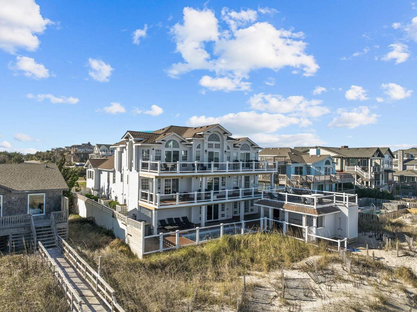Large beachfront house with multiple decks under a blue sky with scattered clouds.