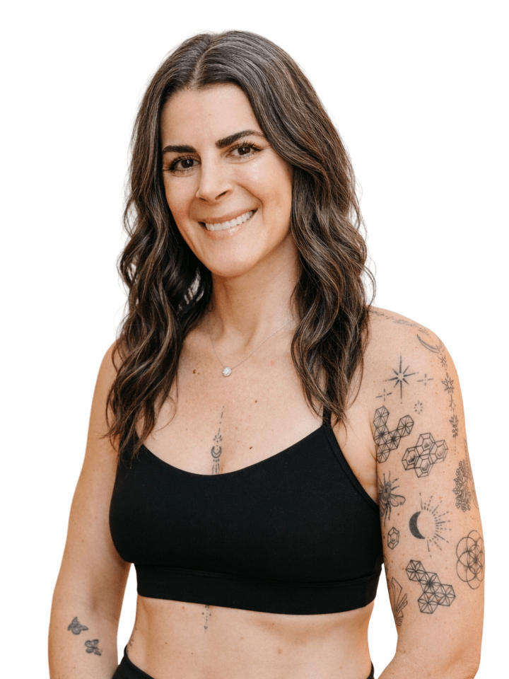Person with wavy hair, tattoos, wearing black top, smiling against white background.