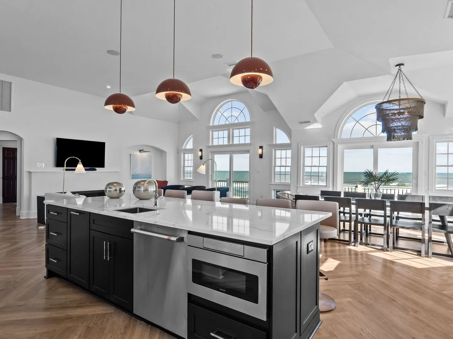 Modern kitchen with large island, pendant lights, and ocean view windows in a bright, open-plan space.