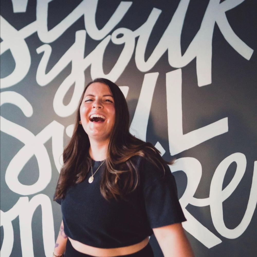 Smiling person in black shirt with white graffiti text background.