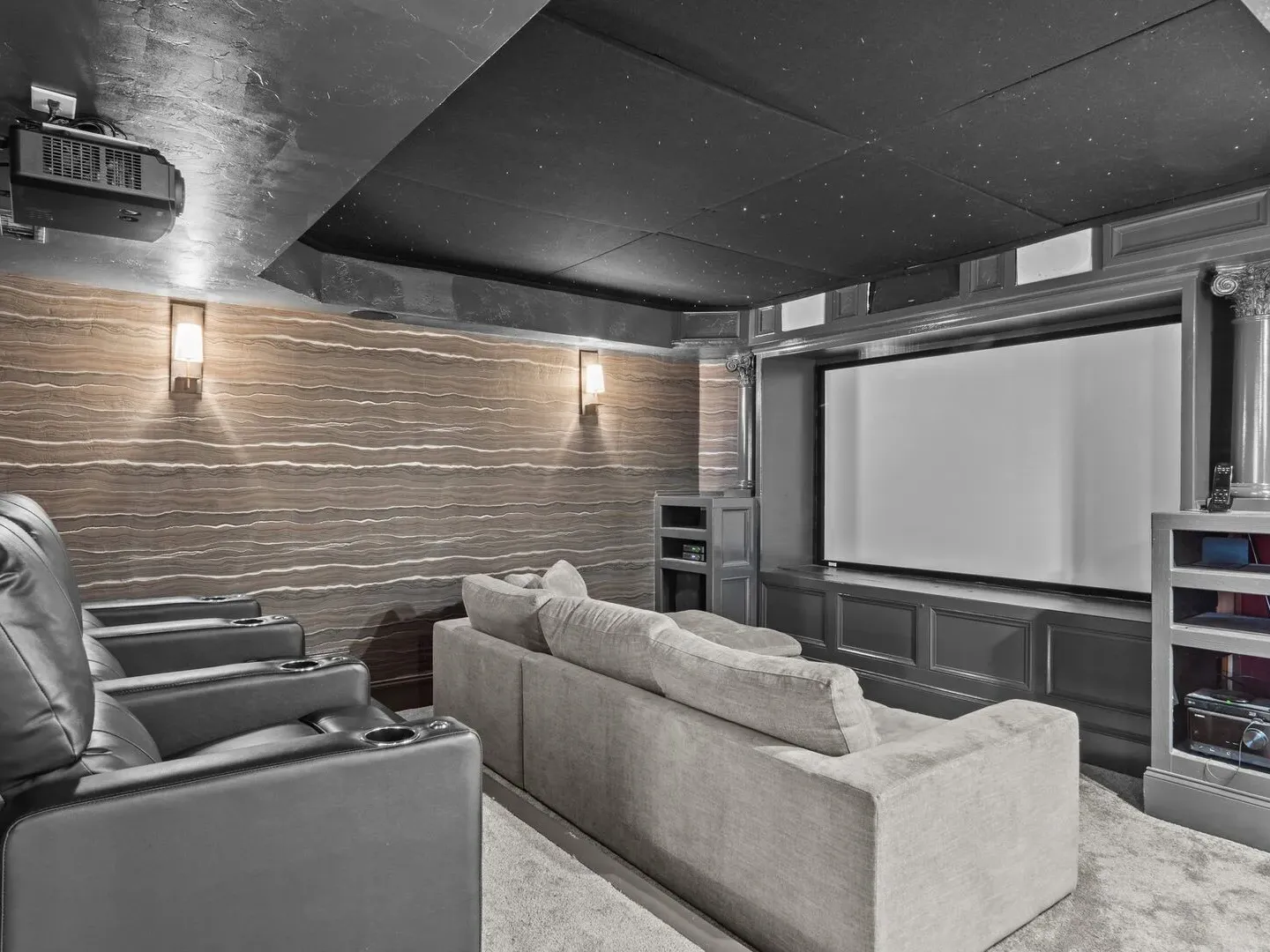 Home theater with gray armchairs, beige couch, ceiling projector, and large screen.