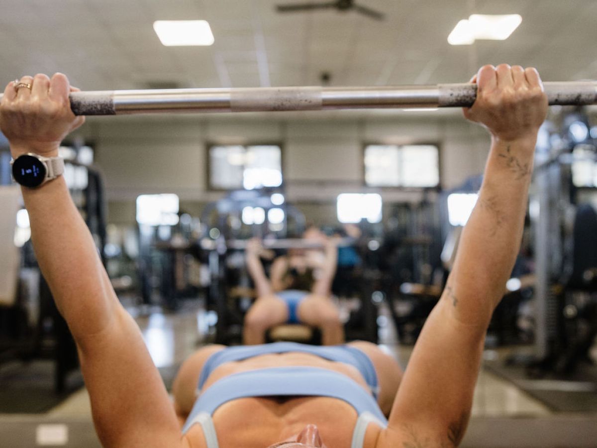 Woman in gym lifting barbell on bench press.